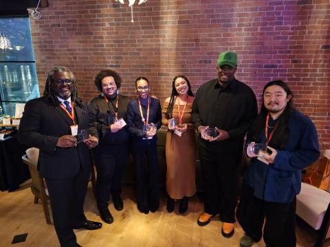 Six folks of color pose together, holding mini statues.