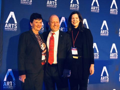 Three people pose in front of a banner with the Arts Advocacy Day logo