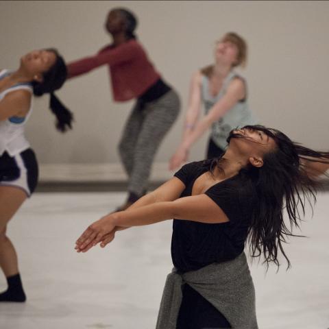 Six dancers, in a studio, throw their heads back. Their hair lays over their faces.