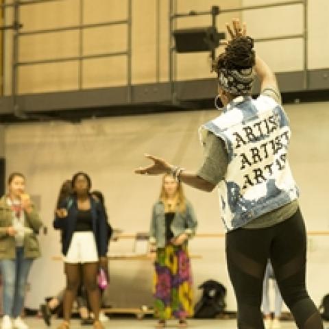 A woman, in a cutoff vest that reads "Artist, Artist, Artist" on the back, speaks with her hands.