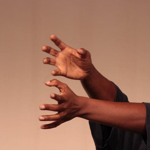 A black person with short green hair wearing a black top reaches, with hands flexed, from the left side of the image