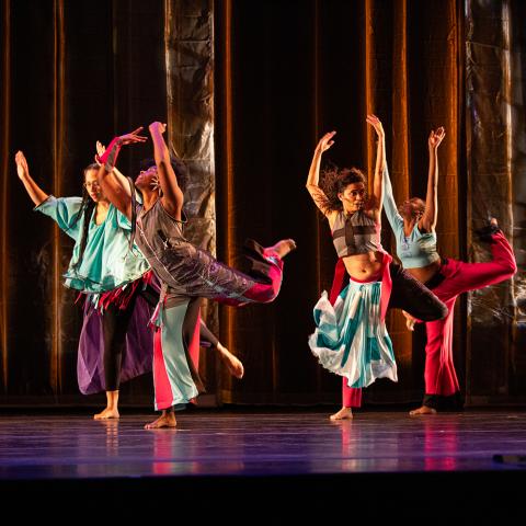 On a stage, five dancers wear color costumes.