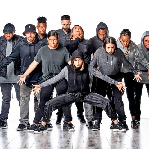 In front of a white backdrop, a crew of 11 folks in grey and black pose.
