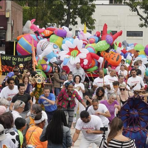 A crowded street with performers and large inflatables.