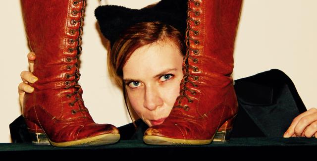 A woman in cat ears peaks around a pair of boots.
