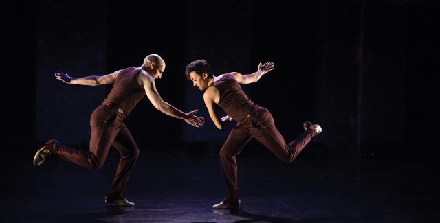 Under a spotlight, two dancers in maroon tank tops and pants perform.