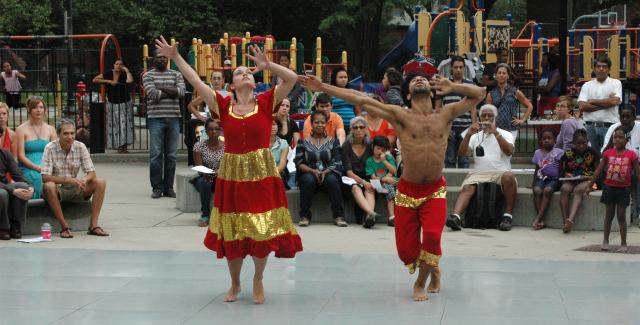 A woman and a man in gold and red stripped costumes perform in a public park.