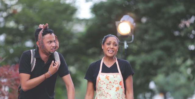 A man, with a rag wrapped around his chin, and a woman in an apron emote under a spotlight.