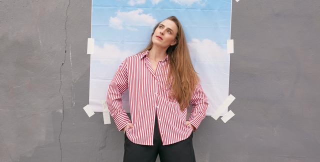 A white, blonde lady poses in front of a small backdrop of clouds that has been taped to the wall.