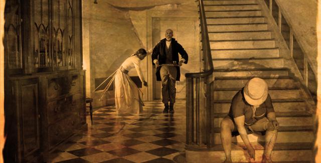 a sepia-tone image of a scene in a grand hallway; a man sits on a staircase, a butler carries a tray, a woman leans onto the butler.