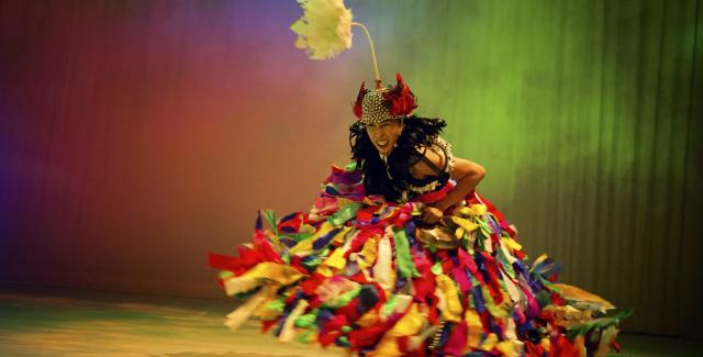 A woman in a multicolored gown dances in a space that reflects multicolored light like a rainbow