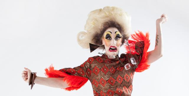 A woman in female drag jumps in front of a white backdrop.