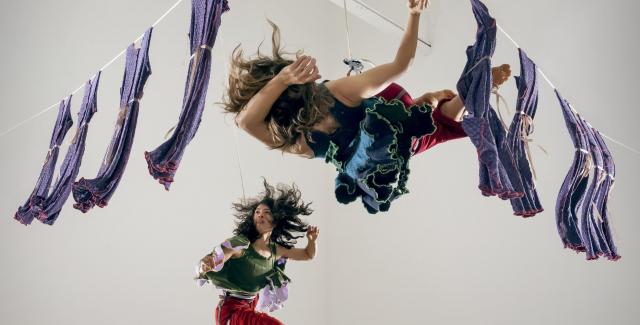 Two women dance between hanging laundry in a white walled studio space.