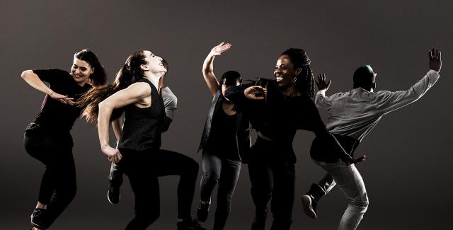 A group of break dancers dance. A couple women in the foreground appear to share a joke.