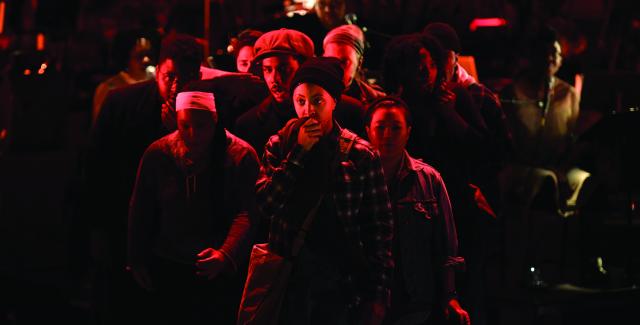 A young person in a crowd of people that appear to be in a riot holds something up to their mouth