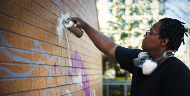 Cedric Douglas spray paints on brick