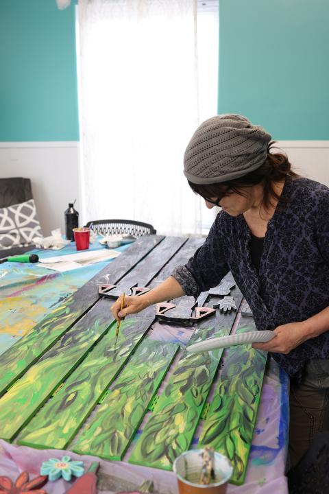 Inside, an artist, in a headwrap, paints boards with a leafy pattern.