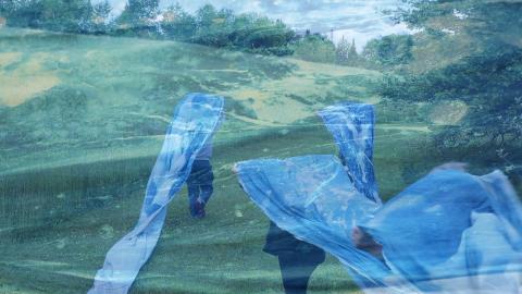 Double exposure. In a field, women carry a blue banner over their heads and a closeup of the blue banner.