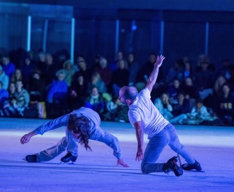 Two male figure skates or ice dancers perform low to the ice.