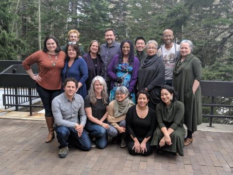 Fifteen people, wearing earth tones, pose and smile.