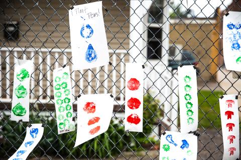 Pieces of paper with shapes painted with stencils hang from a wire fence.