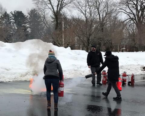 By a snowbank, two people put out a fire with extinguishers.
