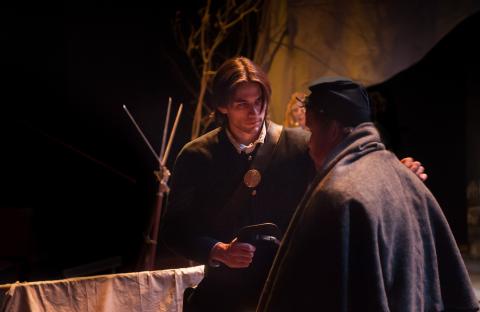 Two actors in civil war era attire have a conversation on a dimly lit stage