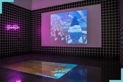 A black tiled gallery has a neon sign on one wall and a projection of the animated image (below) on the other.