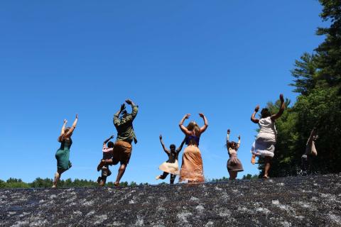 On a sunny day, eight dancers swing and raise their arms.