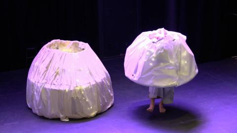 Two folks, dressed round, "egg"-like, fabric costumes stand and sit inside the costumes so you cannot see their heads or torsos. 