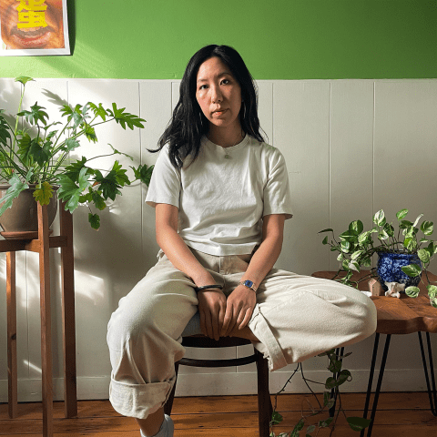 Inside, Lily sits on a stool. She has long brown hair and is Chinese. 