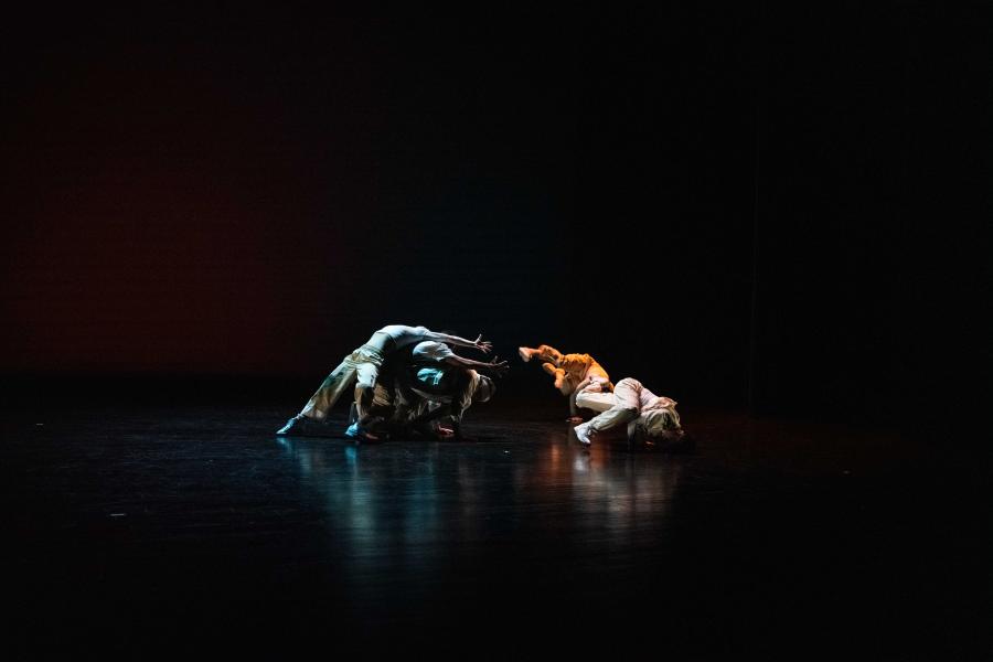 In a dark studio space, two dancers perform in blue light next to two in a yellow spotlight.