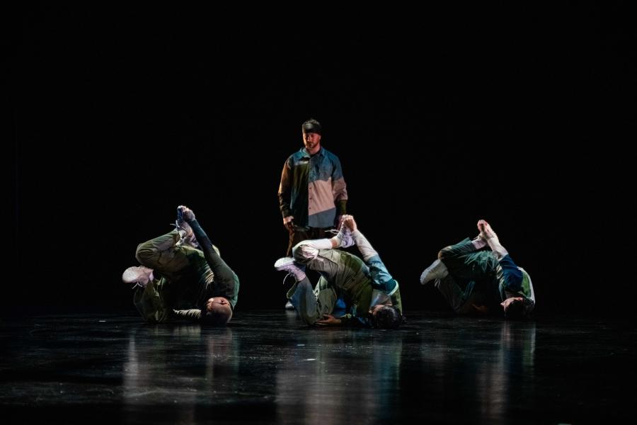 Three dancers do floorwork in front of another dancer who stands and observes.