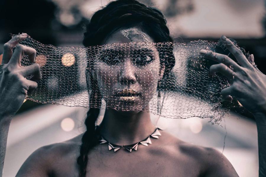 In a stark black and white image, a wide-eyed woman looks through a veil.