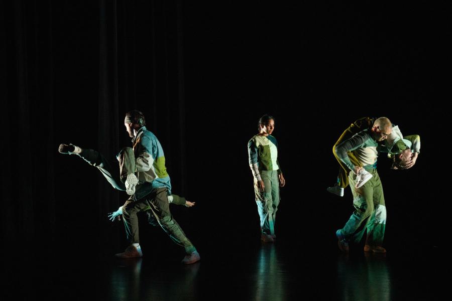 Two dancers carry dancers over their shoulders. They're in color blocked green and blue fabric.