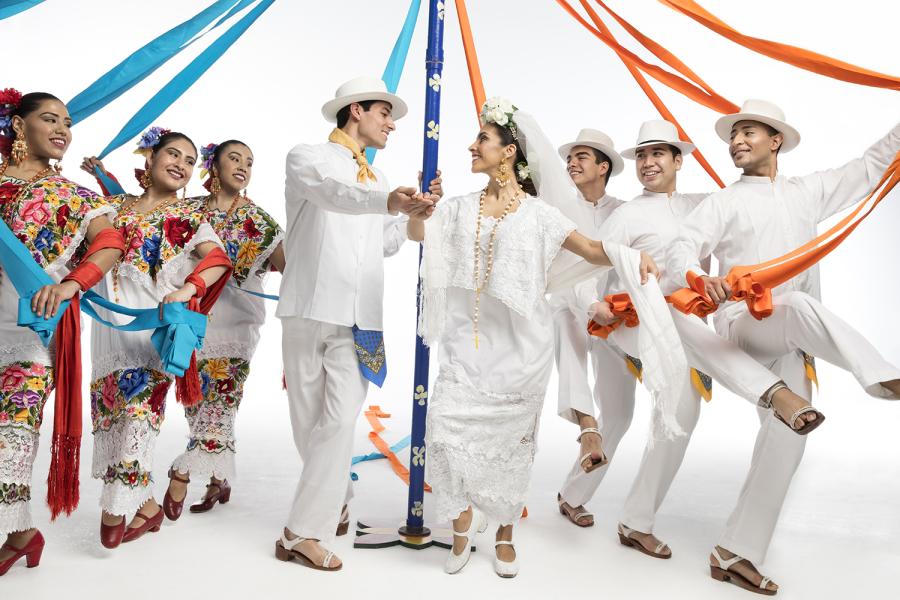 Men and women in traditional Mexican garb dance with ribbons attached to a pole.