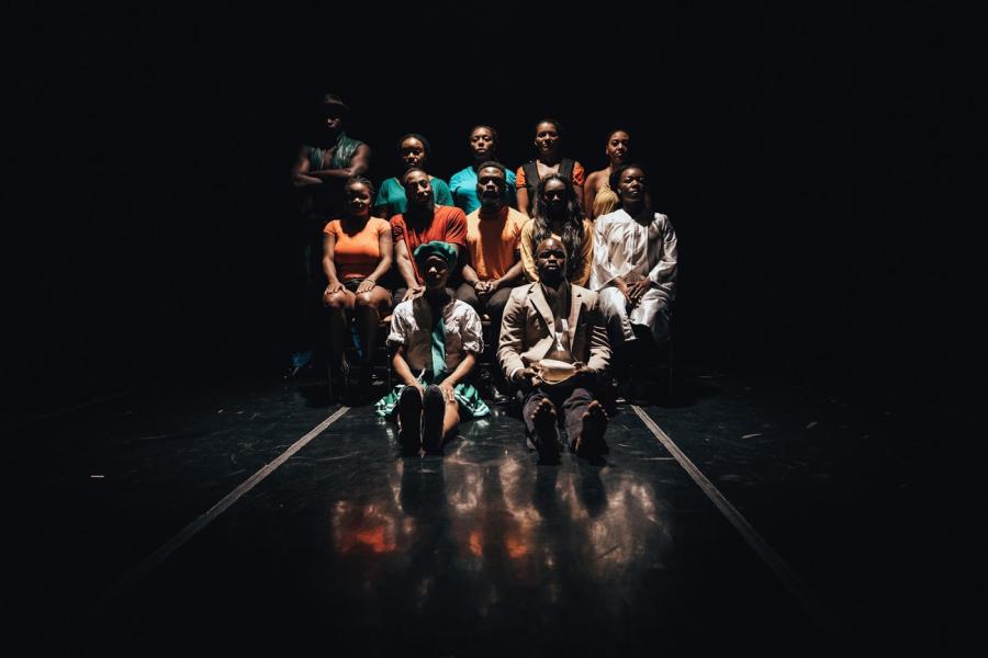 In a dark space, twelve Black folks pose, blank faced.