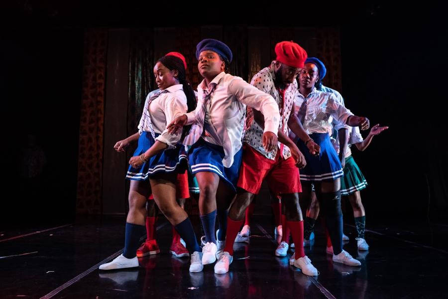 A young Black girls breaks through a crowd of folks in red and blue uniforms dancing.