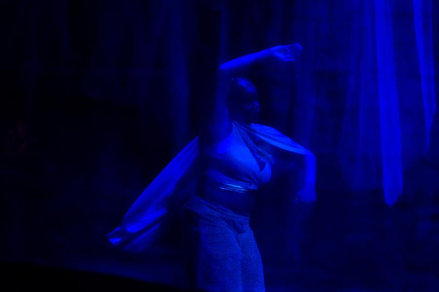 In dim blue blight, a Black woman spins and the fabric of her garments moves with her.