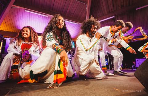 Folks on a stage, in white with color embellishments on their sleeves, are on their knees.