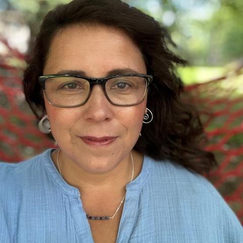 A woman with long dark hair, dark rimmed glasses, and a blue shirt