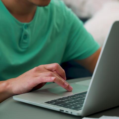 A brown man types on his laptop.