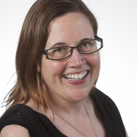 Ann is a white woman with shoulder length brown hair. She smiles and wears glasses, a black v-neck, and a thin silver necklace.