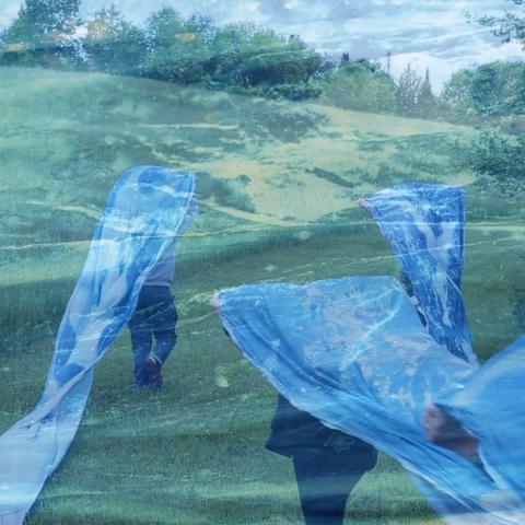 Double exposure. In a field, women carry a blue banner over their heads and a closeup of the blue banner.