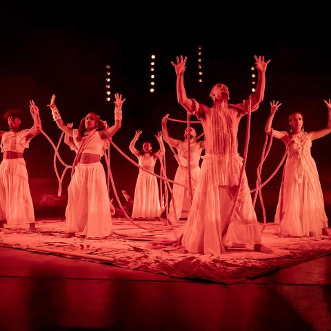 On a stage with red light, dancers hold their palms up.