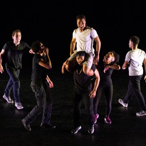Six people dance, with one on another's shoulders.