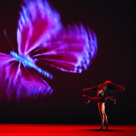 A female dancer spins next to a projection of a very large butterfly.