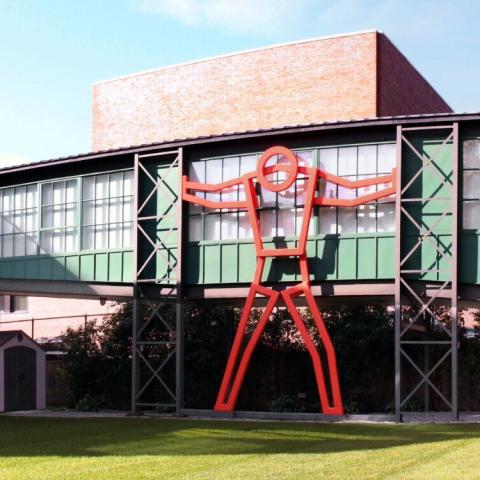 Outside, a museum has a stick figure statue that appears to hold up an indoor bridge.