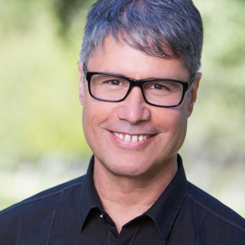 A man with short gray hair and dark framed glasses wearing a dark button down shirt
