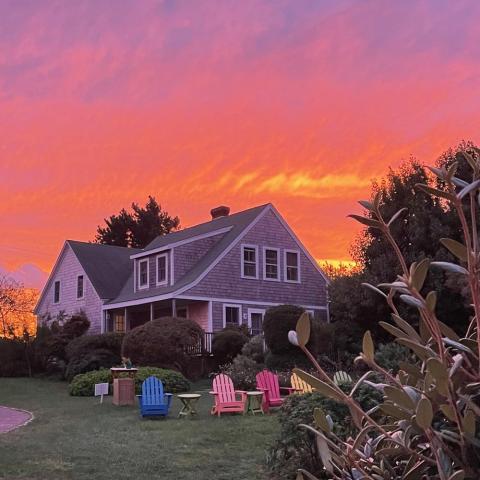 At sunset, a beach house with multi-colored adirondack chairs on the lawn.